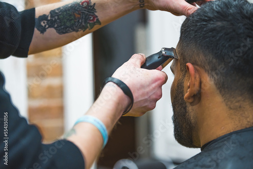 Professional barber with tattoos gromming his client's hair with electric trimmer in a barbershop. . High quality photo photo