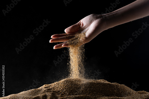 Hand releasing dropping sand. Fine Sand flowing pouring through fingers against black background. Summer beach holiday vacation and time passing concept. Isolated high speed shutter