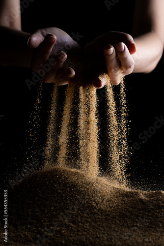 Hand releasing dropping sand. Fine Sand flowing pouring through fingers against black background. Summer beach holiday vacation and time passing concept. Isolated high speed shutter #554355353