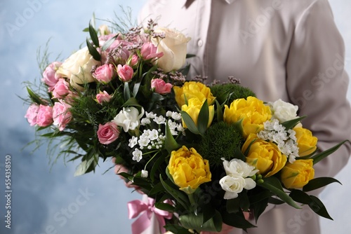 Woman with beautiful bouquets on light blue background, closeup