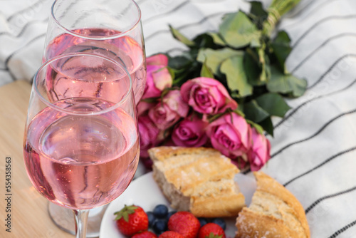 Glasses of delicious rose wine, flowers and food on white picnic blanket, closeup