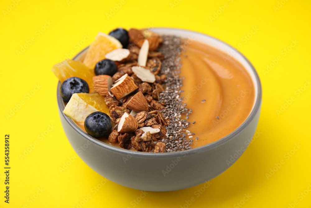 Bowl of delicious fruit smoothie with fresh orange slices, blueberries and granola on yellow background, closeup