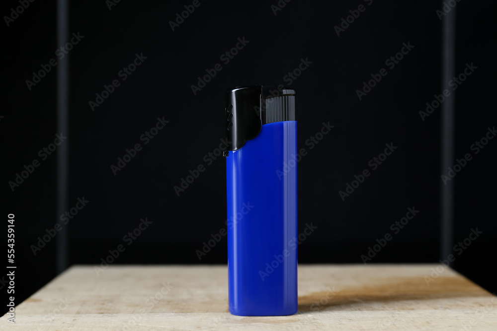 Blue plastic cigarette lighter on wooden table against black background, closeup Blue plastic cigarette lighter on wooden table against black background, closeup