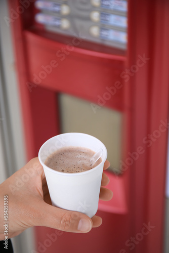 Woman holding paper cup with coffee near vending machine, closeup