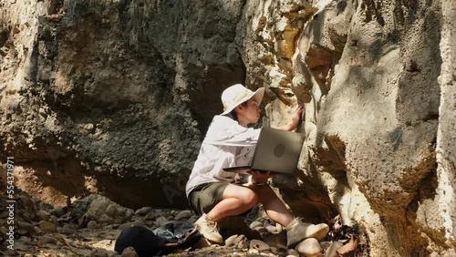 Female geologist using laptop computer examining nature, analyzing rocks or pebbles. Researchers collect samples of biological materials. Environmental and ecology research.