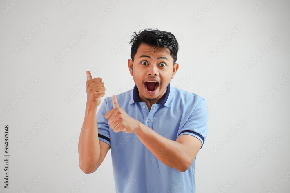 shocked asian man with an open mouth with fingers pointing to behind wearing blue t shirt isolated on white background shocked asian man with an open mouth with fingers pointing to behind wearing blue t shirt isolated on white background