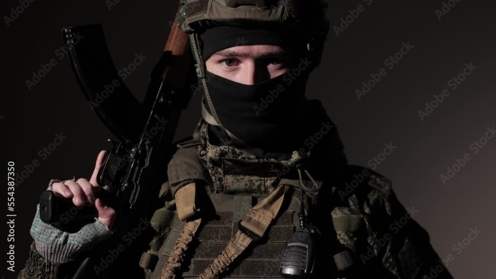 A young military man in uniform looks at the camera. Approaching the camera to the eyes of a military man with gun