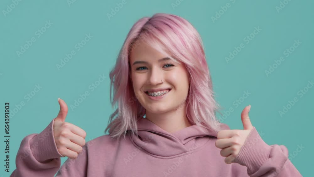 Cheerful Charming beautiful positive young woman with pink hair showing thumbs up, looking happy at camera and enjoying posing on green screen background. Positive feedback, body language sign concept Cheerful Charming beautiful positive young woman with pink hair showing thumbs up, looking happy at camera and enjoying posing on green screen background. Positive feedback, body language sign concept