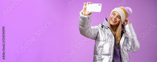 Joyful carefree charming blond girl having fun wanna post pictures from ski resort vacation taking seflie holding smartphone mimicking show tongue winking look mobile display, purple background photo