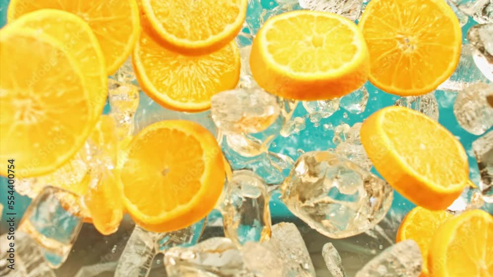 Juicy sweet orange and fly ice cube or water splash or pouring drops juice in super slow motion on 1000 fps. Citrus orange slices and ice fall or explode on blue background, super slow motion 1000fps