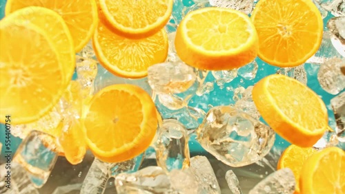 Juicy sweet orange and fly ice cube or water splash or pouring drops juice in super slow motion on 1000 fps. Citrus orange slices and ice fall or explode on blue background, super slow motion 1000fps