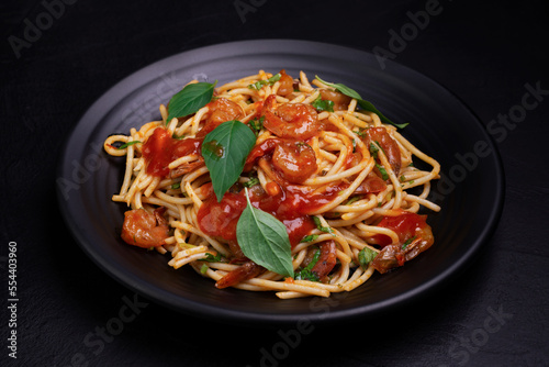 Delicious spaghetti pasta with prawns and cheese served on a black plate. With vegetables, Italian tomato sauce, and spices arranged on a wooden table, black background, top view