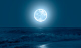 Night sky with blue moon in the clouds over the calm blue sea 