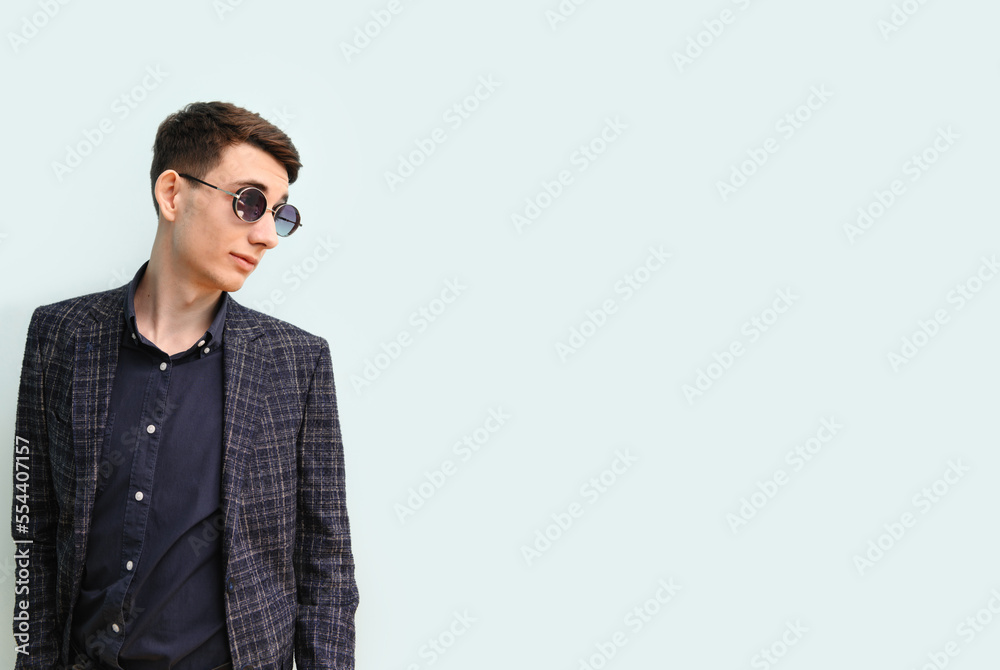 Young man in glasses and stylish clothes standing near a light wall, looking away, banner, place for text