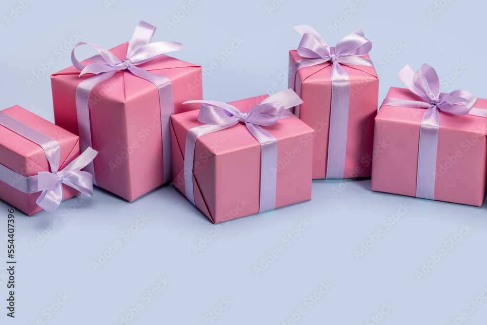 Gifts in pink boxes, decorated with satin ribbon. Concept for greeting card, frame, banner. Blue background, studio shot. Gifts in pink boxes, decorated with satin ribbon. Concept for greeting card, frame, banner. Blue background, studio shot.