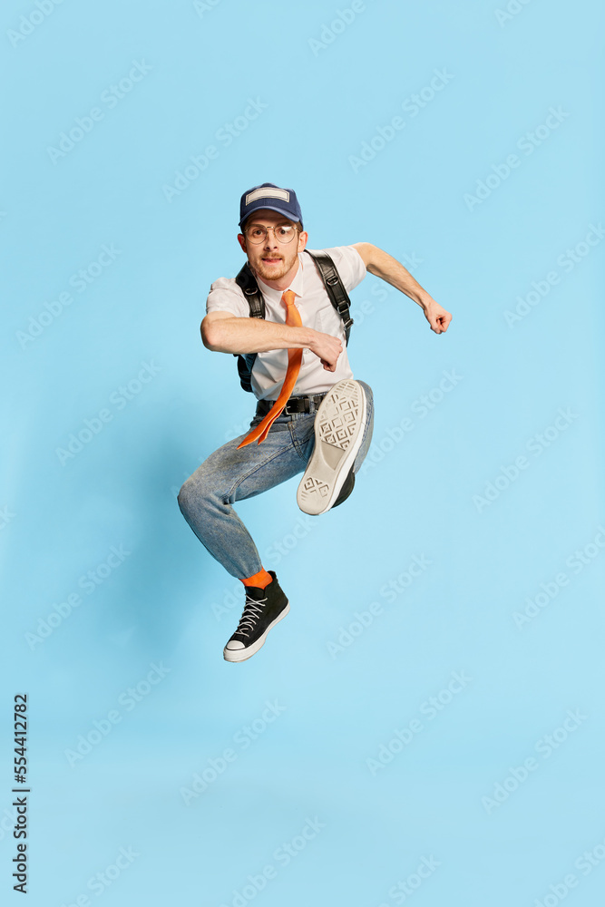 Portrait of young man, student in casual clothes posing isolated over blue background. Hurry up to success