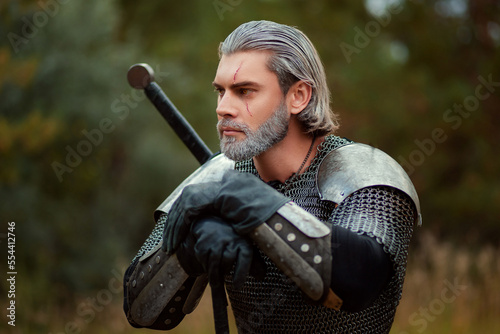An aged male warrior in chain mail with gray hair and a scar on his face. Knight in armor holds a two-handed sword.