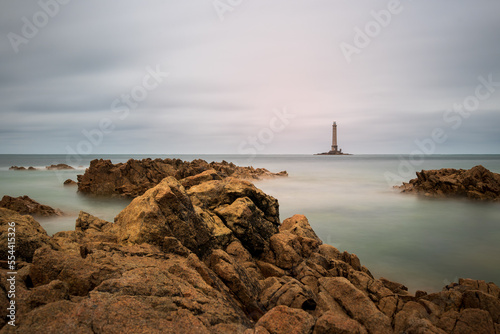 A lighthouse in distance with a rocky sea under cloudy sky