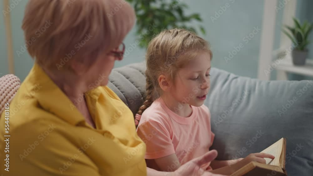 close up elderly woman asks granddaughter to read, a little girl does her homework with her grandmother at home close up elderly woman asks granddaughter to read, a little girl does her homework with her grandmother at home