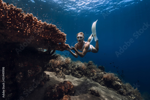 Freediver glides with fins holding on to big coral. Freediving in deep blue ocean with beautiful girl