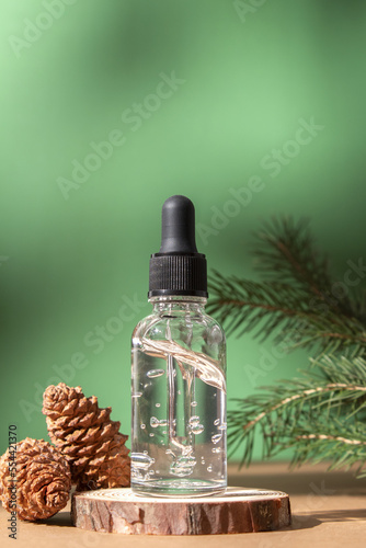 Cosmetic bottle between fir branches and pine cones. Skin care cosmetic. Hyaluronic acid oil, serum with collagen and peptides. Natural cosmetics.