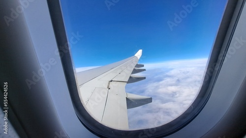 View from the window of the airplane. Rear of the wing. Blue sky. White clouds in the background out of focus. Selective focus. Copy space