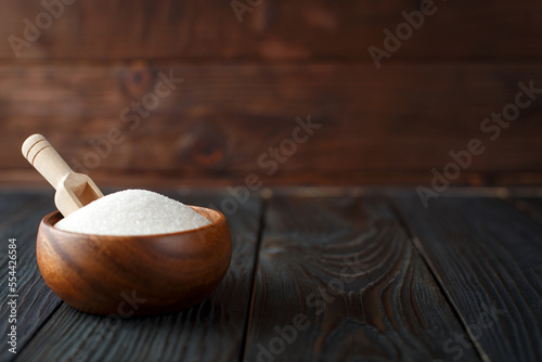 Wooden bowl with sugar on dark wooden background