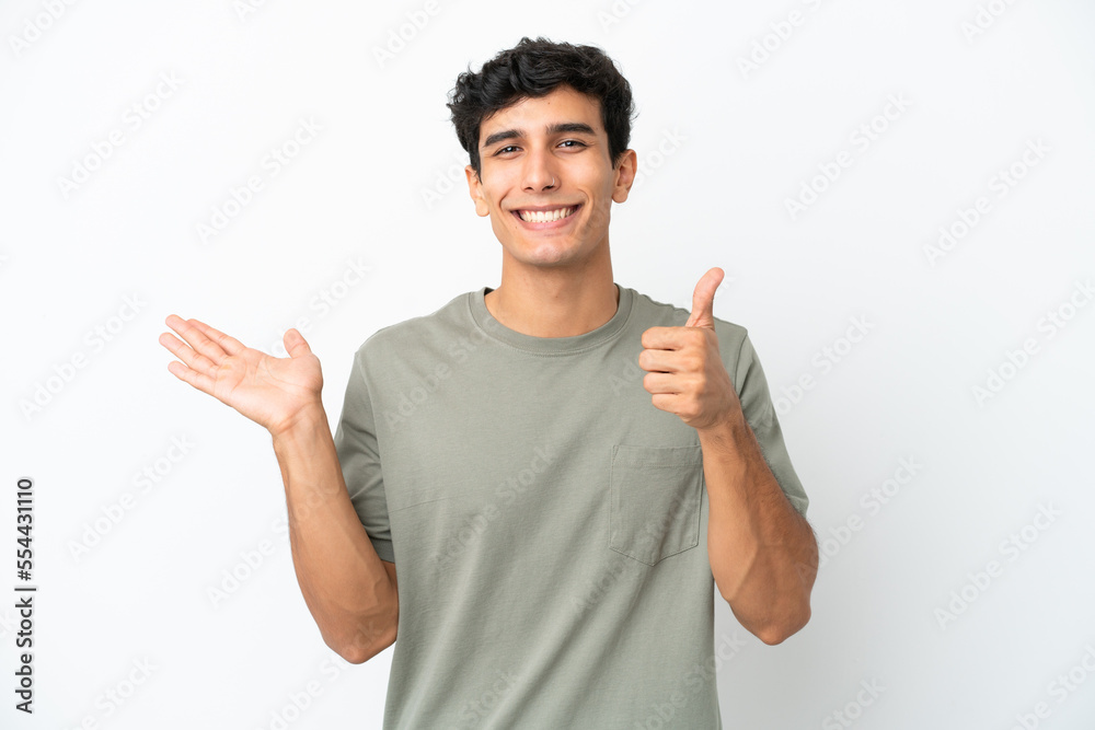 Young Argentinian man isolated on white background holding copyspace imaginary on the palm to insert an ad and with thumbs up Young Argentinian man isolated on white background holding copyspace imaginary on the palm to insert an ad and with thumbs up
