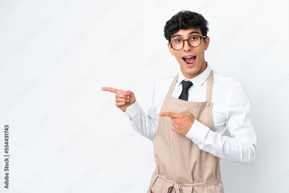 Restaurant Argentinian waiter isolated on white background surprised and pointing side Restaurant Argentinian waiter isolated on white background surprised and pointing side