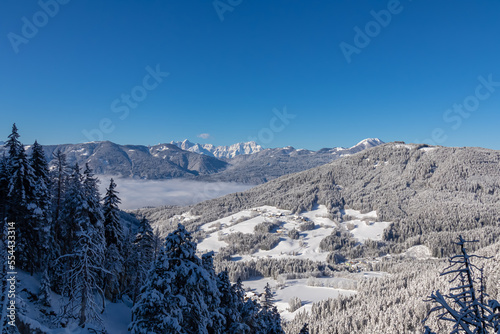 Panoramic view of the snow capped mountain range of Julian Alps seen from Kobesnock near Bad Bleiberg, Carinthia, Austria, Europe. Remote village in winter wonderland on sunny day. Valley full of fog photo