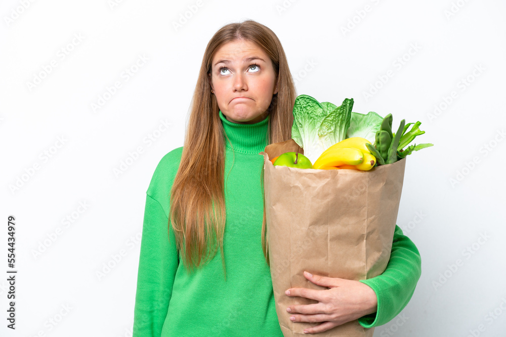 Young caucasian woman holding a grocery shopping bag isolated on white background and looking up Young caucasian woman holding a grocery shopping bag isolated on white background and looking up