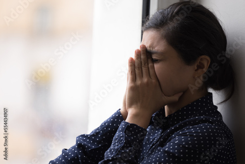Bilde på lerret Frustrated unhappy young Indian woman crying at window, covering face with close