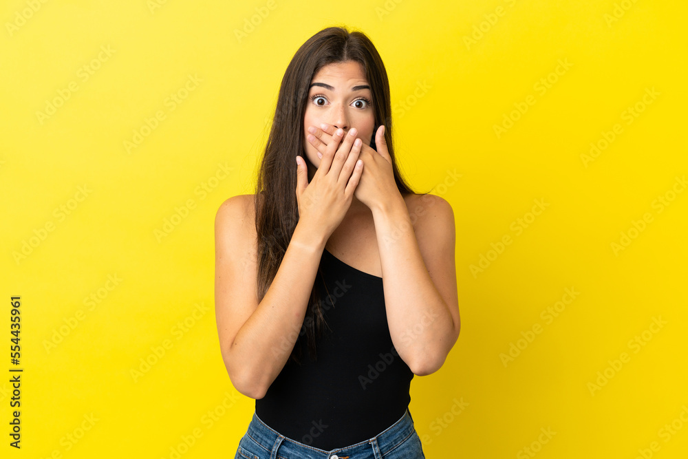 Young Brazilian woman isolated on yellow background covering mouth with hands Young Brazilian woman isolated on yellow background covering mouth with hands