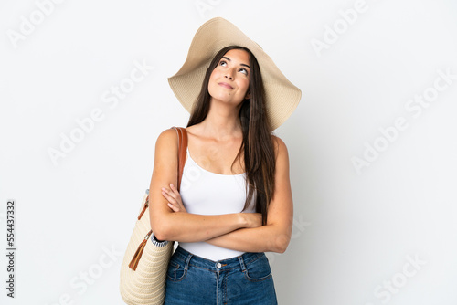 Young Brazilian woman with Pamela holding a beach bag isolated on white background looking up while smiling
