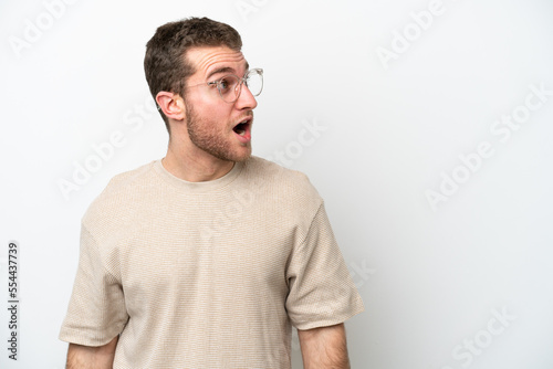Young caucasian man isolated on white background doing surprise gesture while looking to the side