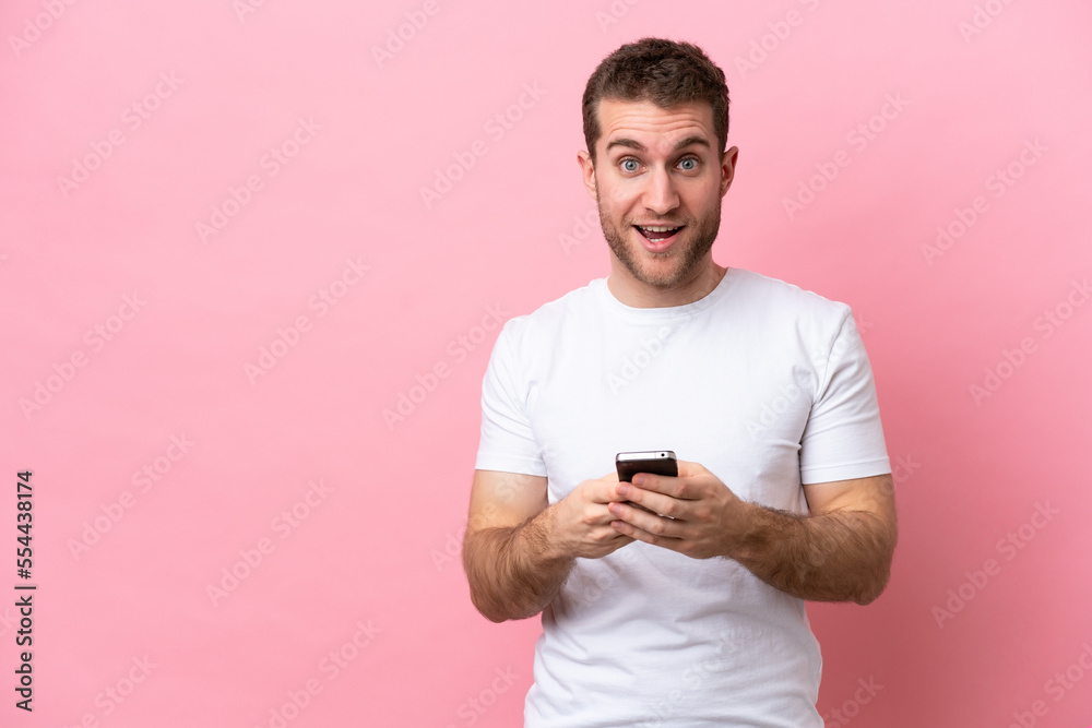Young caucasian man isolated on pink background surprised and sending a message Young caucasian man isolated on pink background surprised and sending a message