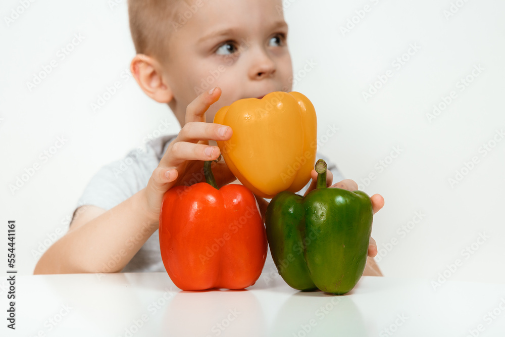 Surprised excited 7s boy, posing fresh peppercorn, looking at camera isolated on white background, studio portrait. Little boy sitting with three paprika of red, green, yellow colors. Surprised excited 7s boy, posing fresh peppercorn, looking at camera isolated on white background, studio portrait. Little boy sitting with three paprika of red, green, yellow colors.