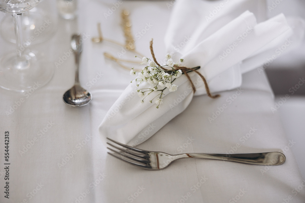 Wedding. Decor. Banquet. A table with a white tablecloth in the festive hall is decorated with a composition of flowers and greenery, there are candles, glasses, cutlery and name plates for guests Wedding. Decor. Banquet. A table with a white tablecloth in the festive hall is decorated with a composition of flowers and greenery, there are candles, glasses, cutlery and name plates for guests