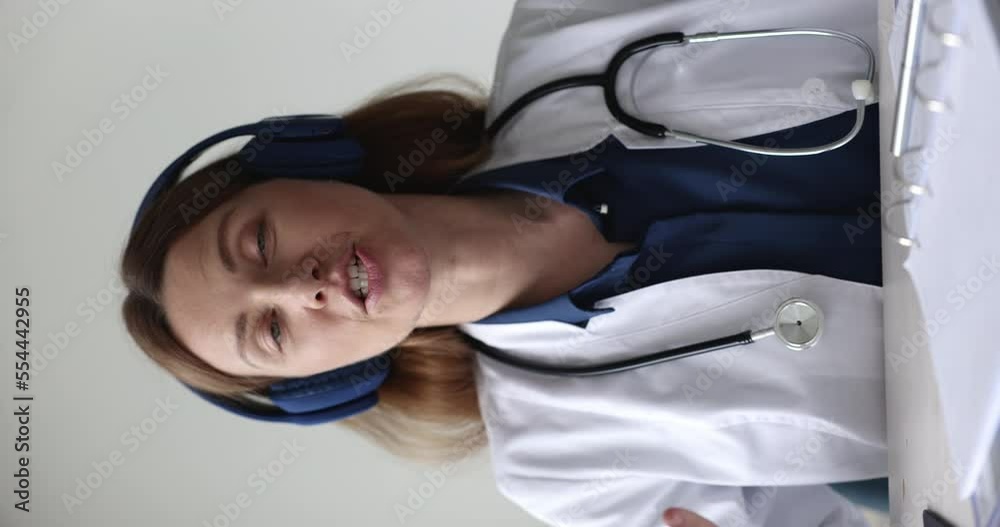 Modern tech usage, telemedicine, on-line healthcare services. Vertical view young 35s female GP in white coat looks at cam start videoconference talk to client, provide helpful info, support remotely Modern tech usage, telemedicine, on-line healthcare services. Vertical view young 35s female GP in white coat looks at cam start videoconference talk to client, provide helpful info, support remotely