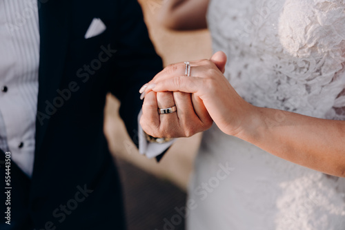 Wedding. The groom in a suit and the bride in a white dress hold hands. Wedding rings on fingers.