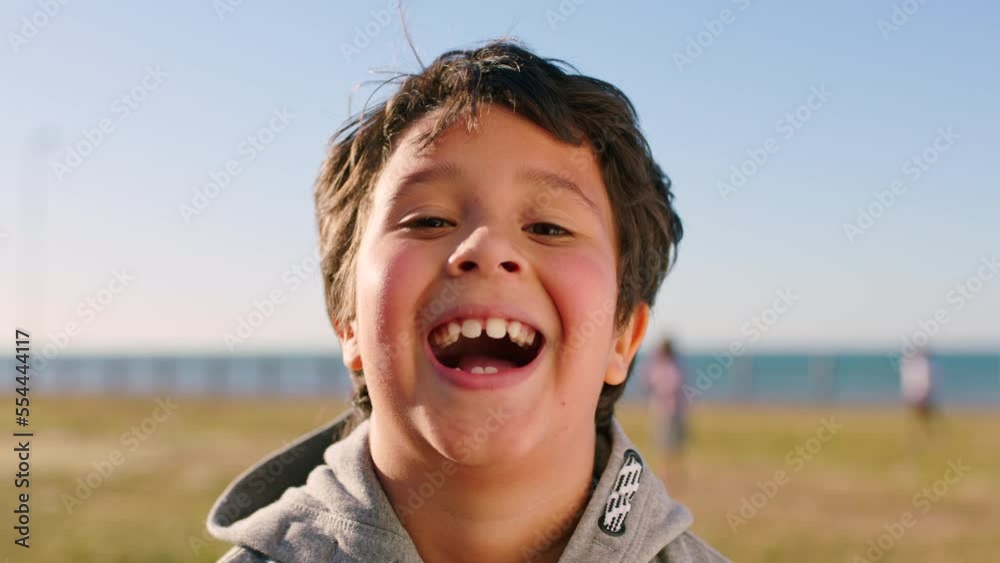 Laughing face, kid and boy portrait from Florida by the sea on a field ready for outdoor play. Comic, happiness and smile of a child on summer holiday by the ocean feeling happiness from vacation