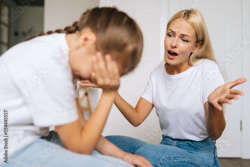 Close-up of sad depressed little girl crying covering face with palm while angry young mother scolding, raising voice, scream at stubborn difficult little child daughter for bad behavior at home.