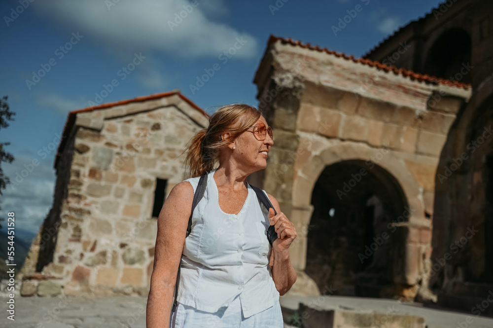 Elderly smiling senior traveling woman backpacker tourist walking posing outdoors in ancient Europe fortress ruins. Retired mature people summer holiday vacation, active lifestyle concept