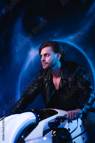 A handsome cyberpunk man in the dark sits on a space motorcycle. A guy in a leather jacket in the scenery of the future in neon color flies through space.