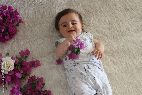 Cute baby play with begonvil flower and smiling on white fluffy blanket. photo