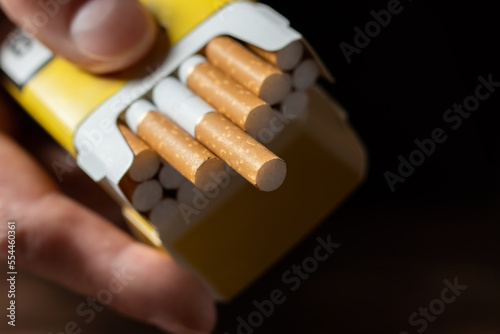 A mans hand holding out an open pack of cigarettes