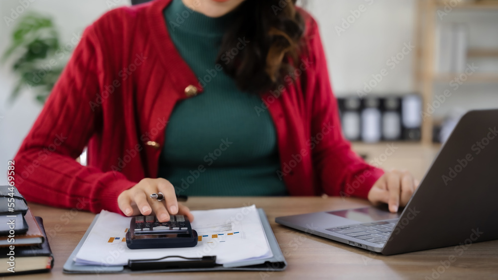 women use the calculator and take notes with calculations about the expenses at the office.
