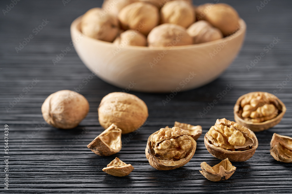 walnuts spill out of a wooden bowl on a black table, selective focus. walnuts spill out of a wooden bowl on a black table, selective focus.