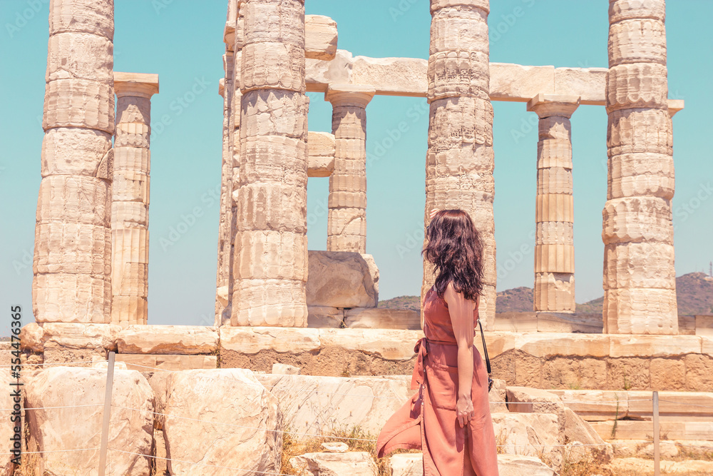 A young girl in a brown summer dress looking at the ancient temple of Poseidon on the Cape Sounion, closeup