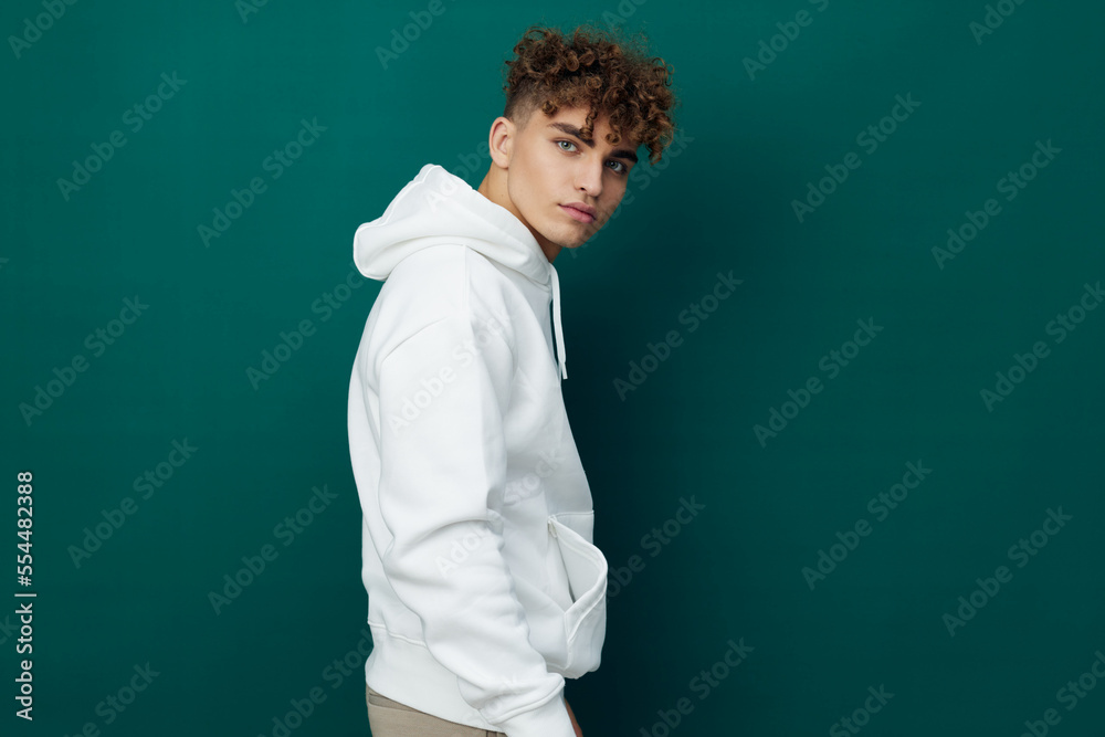 a cute, funny, joyful man stands on a green background in a white hoodie and looks pleasantly into the camera, turning sideways. Horizontal studio photo for inserting an advertising layout